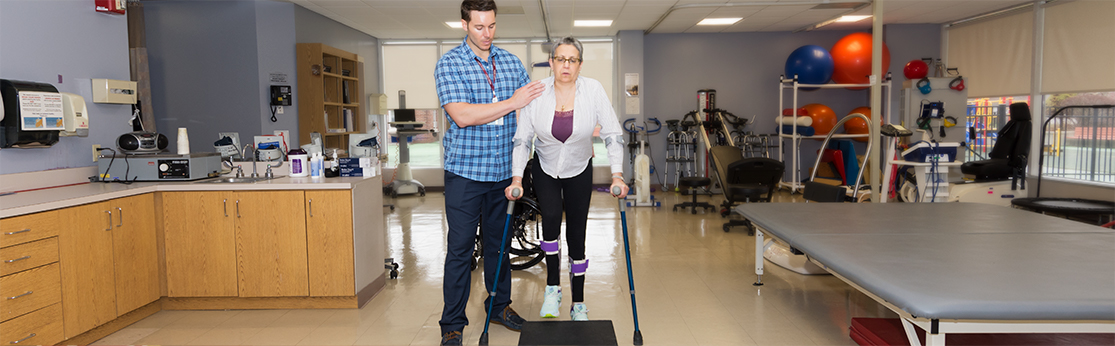 Patient using forearm crutches stepping up onto a step box with a physical therapist supporting her shoulder and back