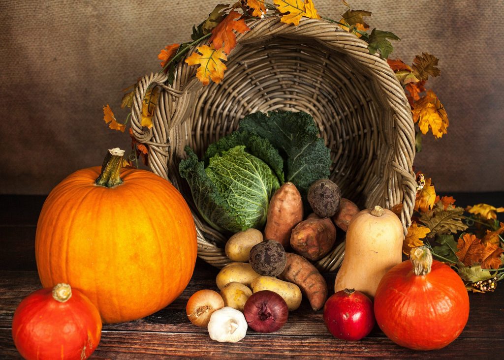 Basket set on its side with pumpkins, potatoes, lettuce, squash, onions, garlic, and turnips pouring from it