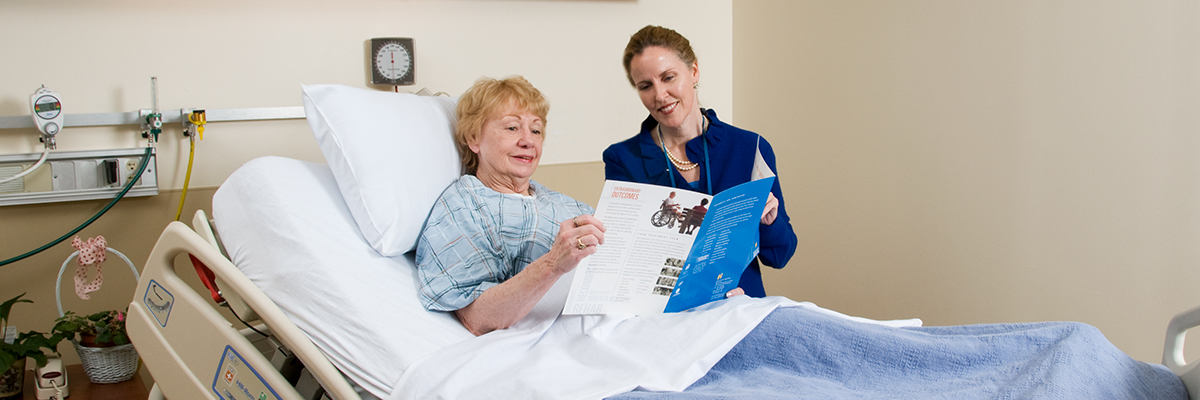 Patient in hospital bed and and employee reviewing a pamphlet with her