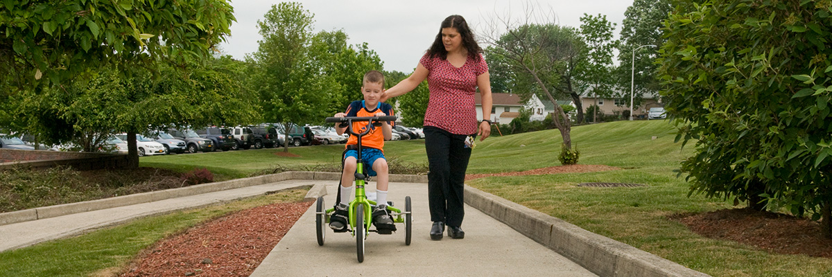 Physical Therapist walking alongside pediatric patient on a bike outside