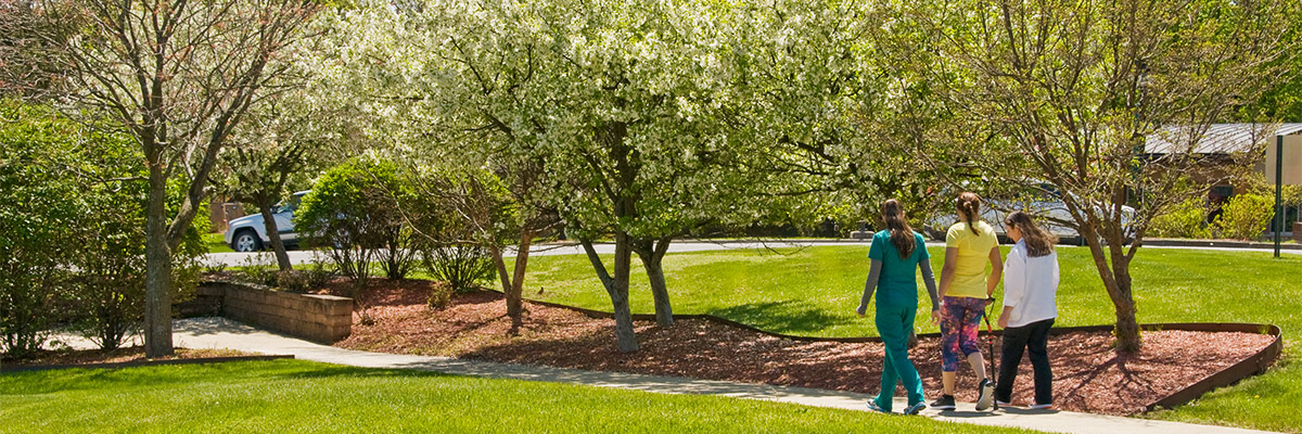 Female patient walking outdoors with cane and physical therapist and assistant