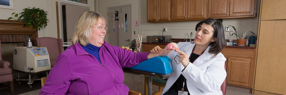 Hand therapist and patient seated and working on hand therapy on the patient's left hand