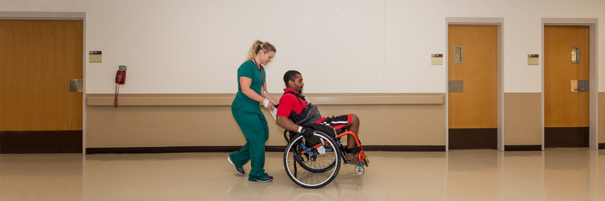 Nurse assisting patient in wheelchair down a hallway