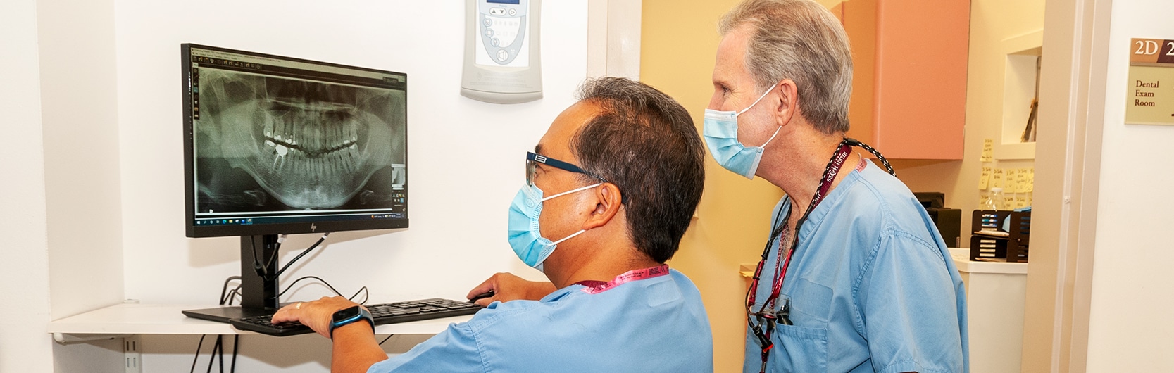 Dr. Nestor Santos sitting and Dr. Marc Michalowicz standing and reviewing a tooth X-ray on a computer screen
