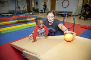 Female therapist with a female toddler pediatric patient rolling a ball up an incline