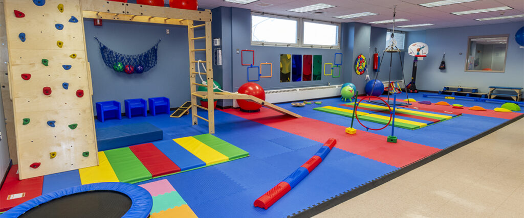 Photo of colorful pediatric gym, featuring multicolored matts, balls, a climbing gym, and other therapeutic equipment for pediatric patients.